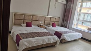 Una habitación de hotel con dos camas, un ventanal con cortinas, un aire acondicionado montado en la pared y una mesita.