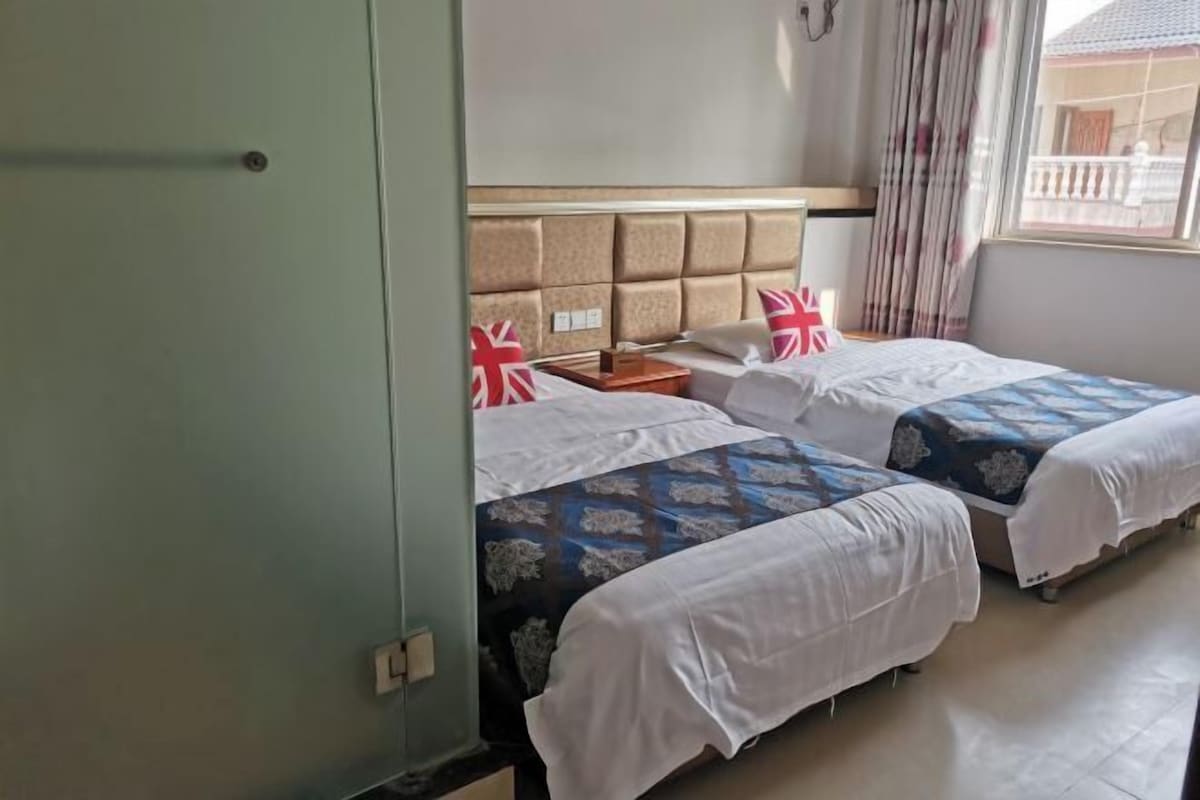 Ein Hotelzimmer mit zwei Betten, einem Kopfteil, einem Nachttisch und einem Fenster mit Vorhängen.
