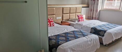 Quarto de hotel com duas camas, cabeceira, mesa de cabeceira e janela com cortinas.