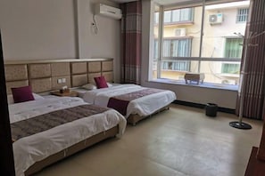 Habitación de hotel con dos camas, ventana con vista a edificios, equipo de aire acondicionado y una pequeña mesa.