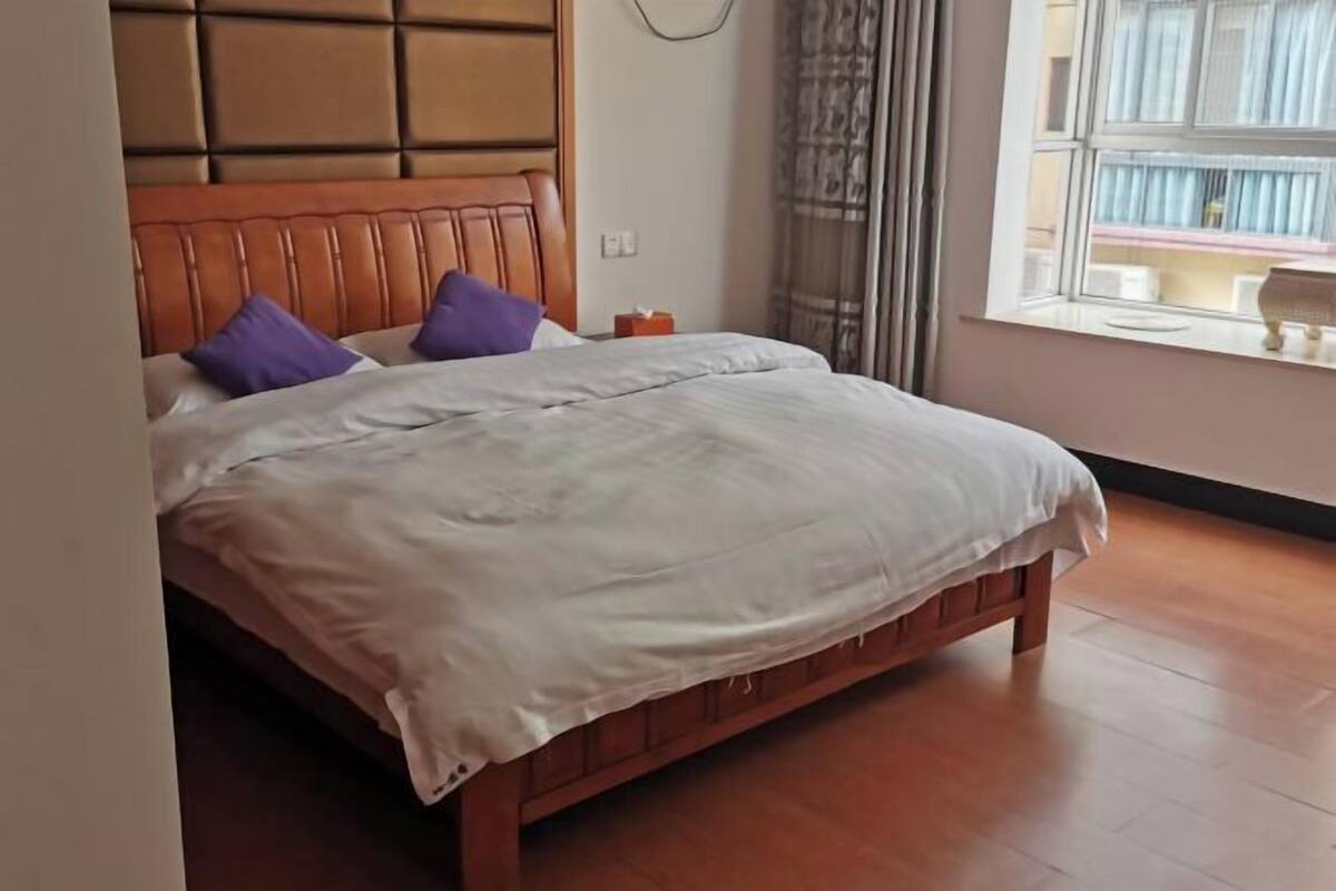 A bed with a wooden headboard, white bedding, and purple pillows.