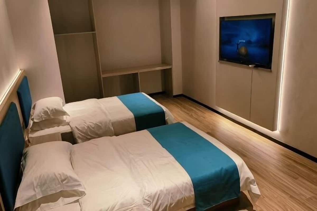 A room with two beds, a TV on the wall, and a wooden floor.