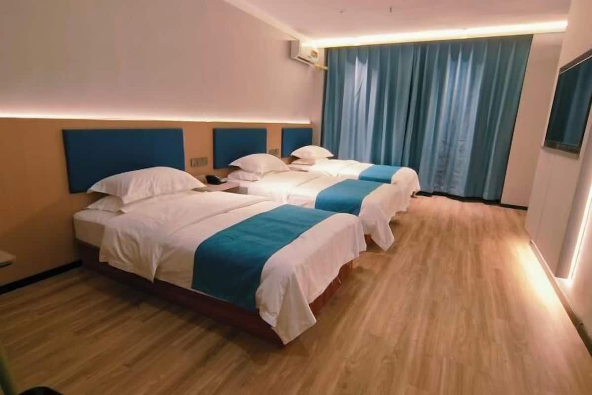 A hotel room with two beds, a wooden floor, a blue curtain, and a flat-screen TV.