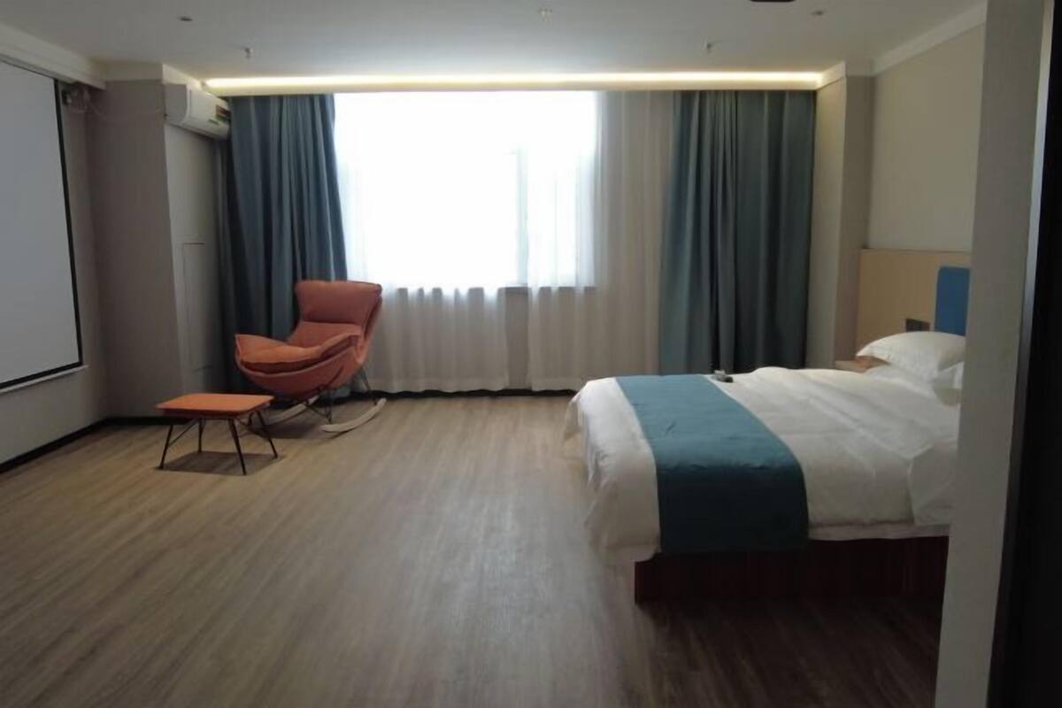 A hotel room with a bed, a chair, a small table, and a large window with curtains.