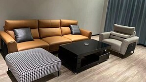 Ein stilvolles Wohnzimmer mit einem braunen Ledersofa, einem schwarzen Couchtisch, einem gemusterten Ottomanen und einem beigefarbenen Sessel.
