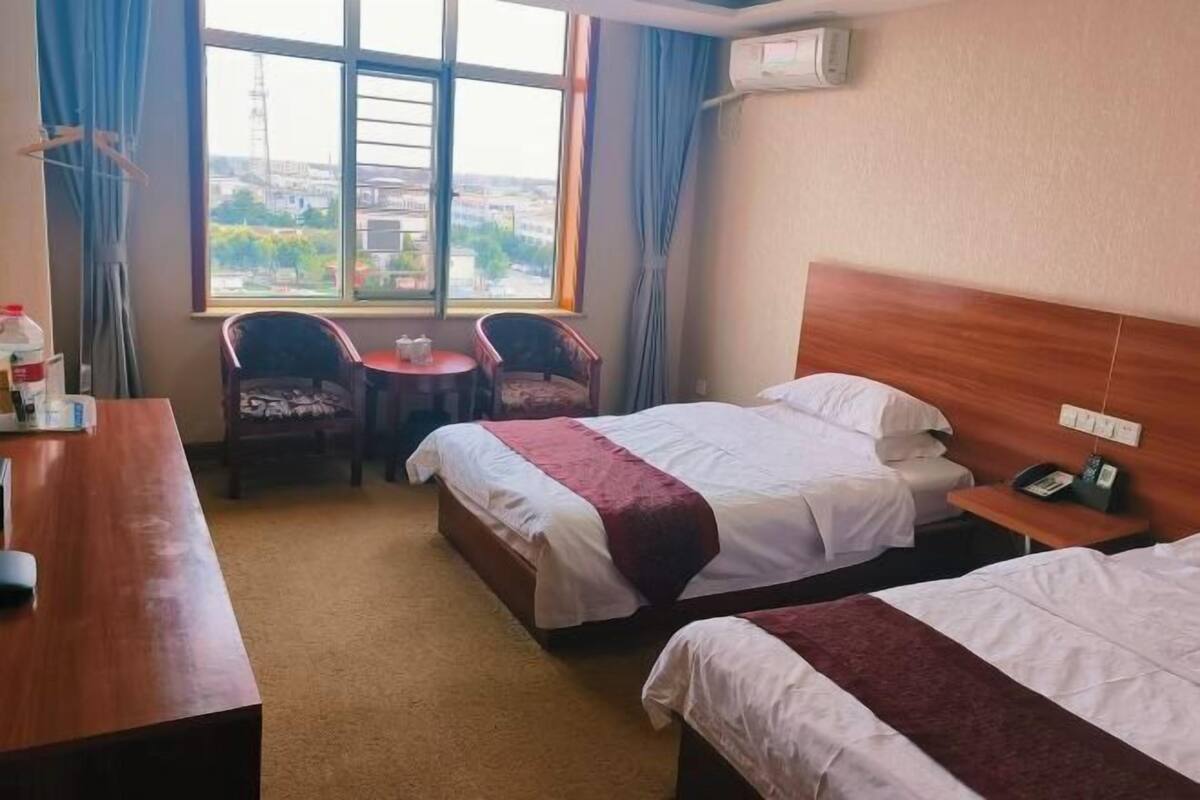 A hotel room with two beds, a desk, a chair, a small table, and a window with curtains.
