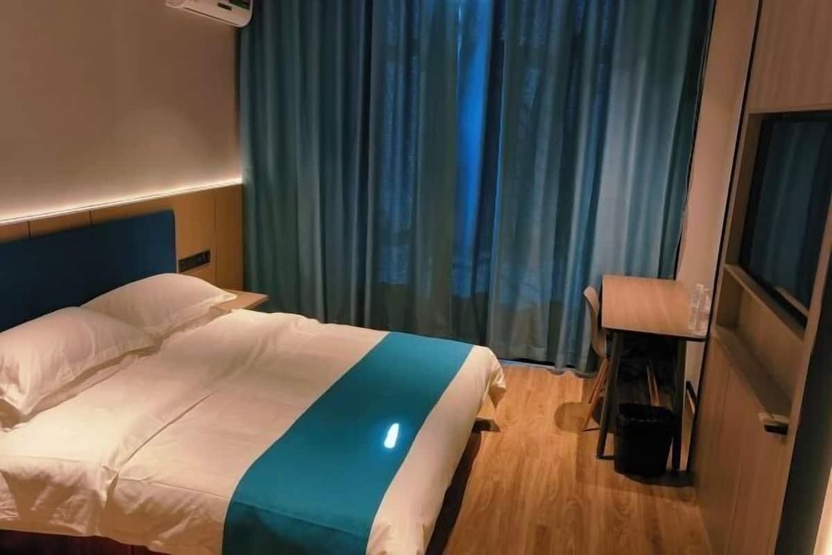 A hotel room with a bed, a desk, a chair, a TV, and a window with curtains.