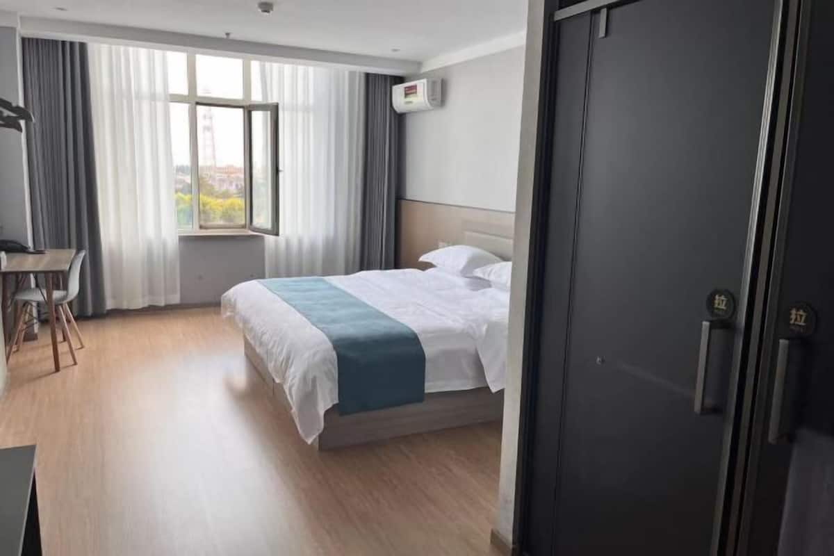 A hotel room with a bed, a desk, a chair, a window with curtains, and a door.