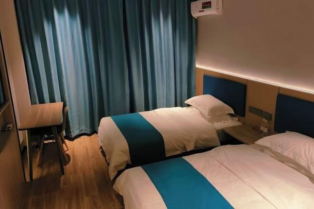 A hotel room with two beds, a small table, and a curtain.