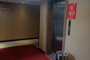 An elevator with a red emergency exit sign, a metal trash bin, and a wall with a fire safety sign. - Fuqing New Port Express Hotel (Fuqing)