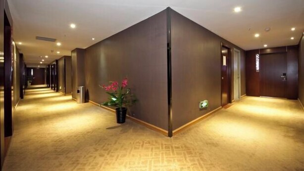 A hotel corridor with a carpeted floor, a plant, and a door at the end. - Fuqing New Port Express Hotel (Fuqing)