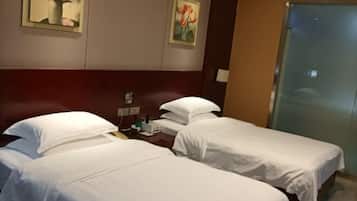 A hotel room with two single beds, a wooden headboard, a small table with a lamp, and two paintings on the wall.