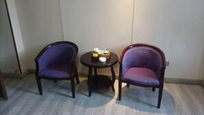 Two purple upholstered chairs and a small round table with a tray of items in a room with light-colored walls and a wooden floor. - Fuqing New Port Express Hotel (Fuqing)