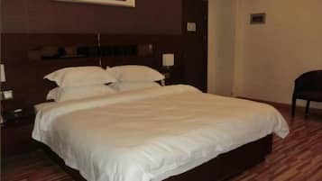 A hotel room with a large bed, a wooden headboard, a nightstand, and a chair.