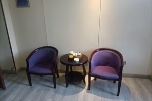 Two purple upholstered chairs, a small round table with a tea set, and a plain wall with a door on the left. - Fuqing New Port Express Hotel (Fuqing)