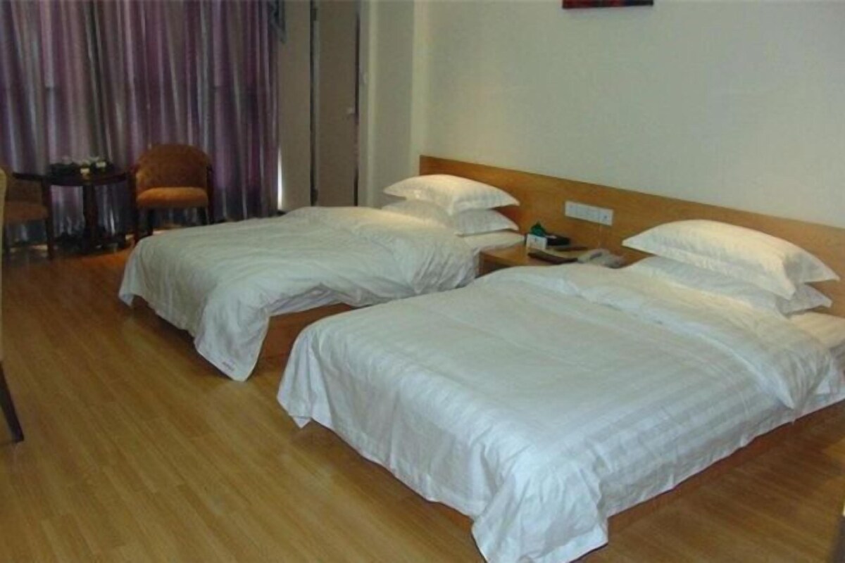 A hotel room with two single beds, a wooden floor, a small table, and a chair.