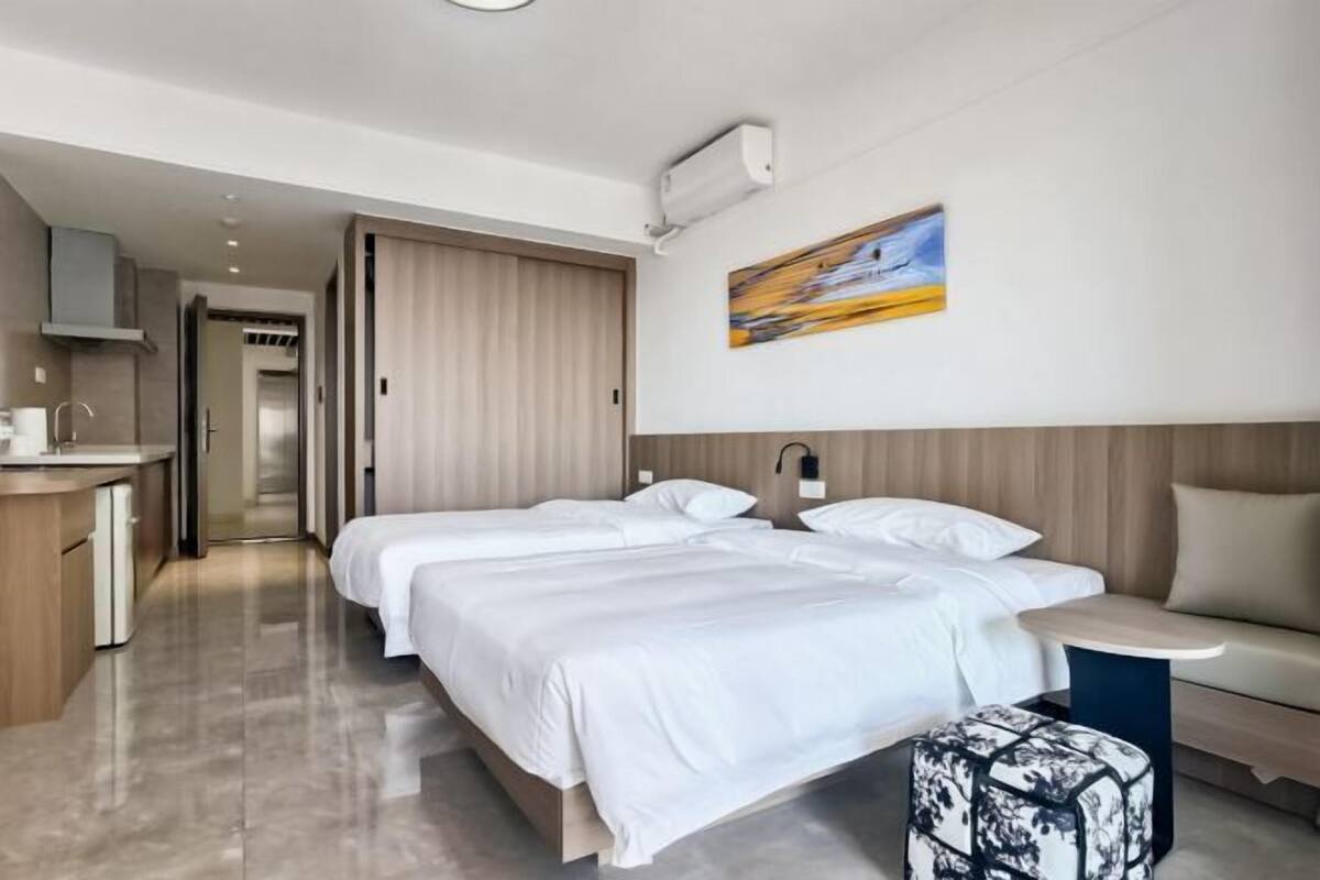 Une chambre d’hôtel moderne équipée de deux lits, d’un canapé, d’une petite table, d’un tableau et d’une kitchenette.