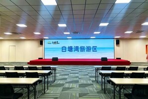 Une salle de conférence équipée d’une scène, d’un écran de présentation, ainsi que de plusieurs rangées de tables et de chaises.