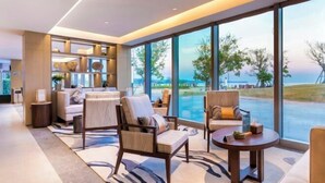 A modern hotel room with a large window offering a view of the beach, a sofa, two armchairs, and a small round table. - Amoy Bay Tourist Restort (Zhangzhou)
