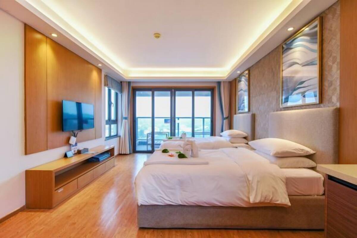 Une chambre d’hôtel moderne dotée d’un grand lit, d’un téléviseur à écran plat, d’une console en bois et d’une grande fenêtre offrant une vue sur la ville.
