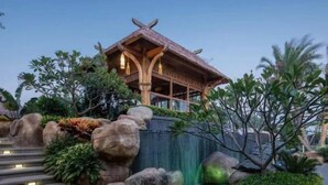 A traditional wooden pavilion with a thatched roof, surrounded by landscaped rock formations and greenery. - Amoy Bay Tourist Restort (Zhangzhou)