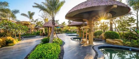 A resort pathway with palm trees, a water feature, and thatched-roof structures.