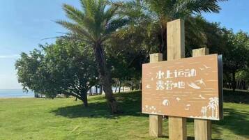 A wooden sign with text, set against a backdrop of palm trees and a grassy area.
