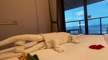 A hotel room with a bed, a window with a view of the beach, and a flower on the bed.