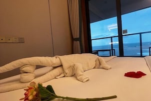 Habitación de hotel con una cama, ventana con vista a la playa y una flor sobre la cama.