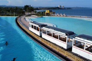 Eine Wasserrutsche mit einer bootförmigen Struktur, einem Pool und einem Strand im Hintergrund.