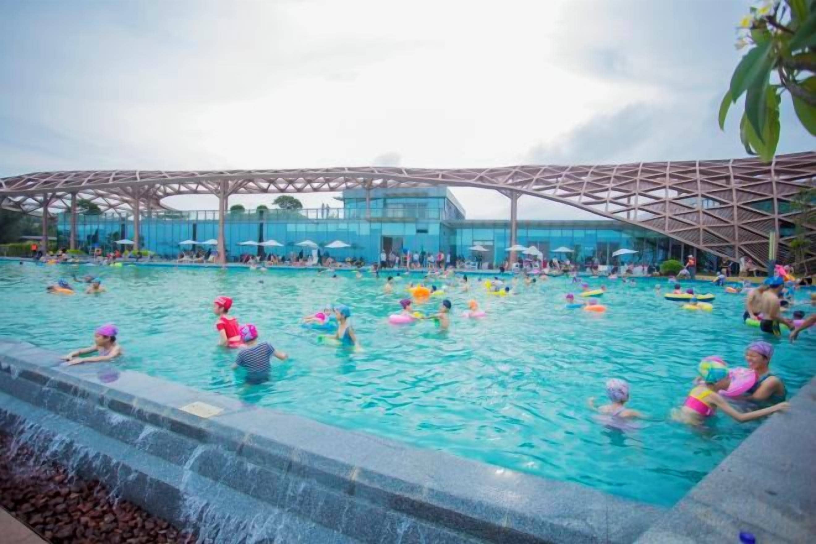 A swimming pool with people, a covered area, and a building in the background.