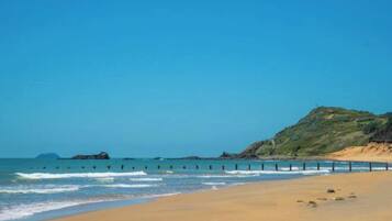 A beach with a sandy shore, a rocky outcrop, and a clear blue sky.