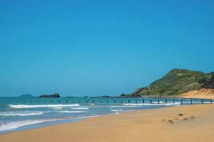 Una playa con arena, un promontorio rocoso y un cielo azul despejado.