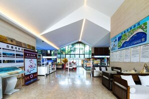 Un hall d’entrée spacieux avec un plafond haut, un comptoir d’accueil, un espace salon et des panneaux d’information.