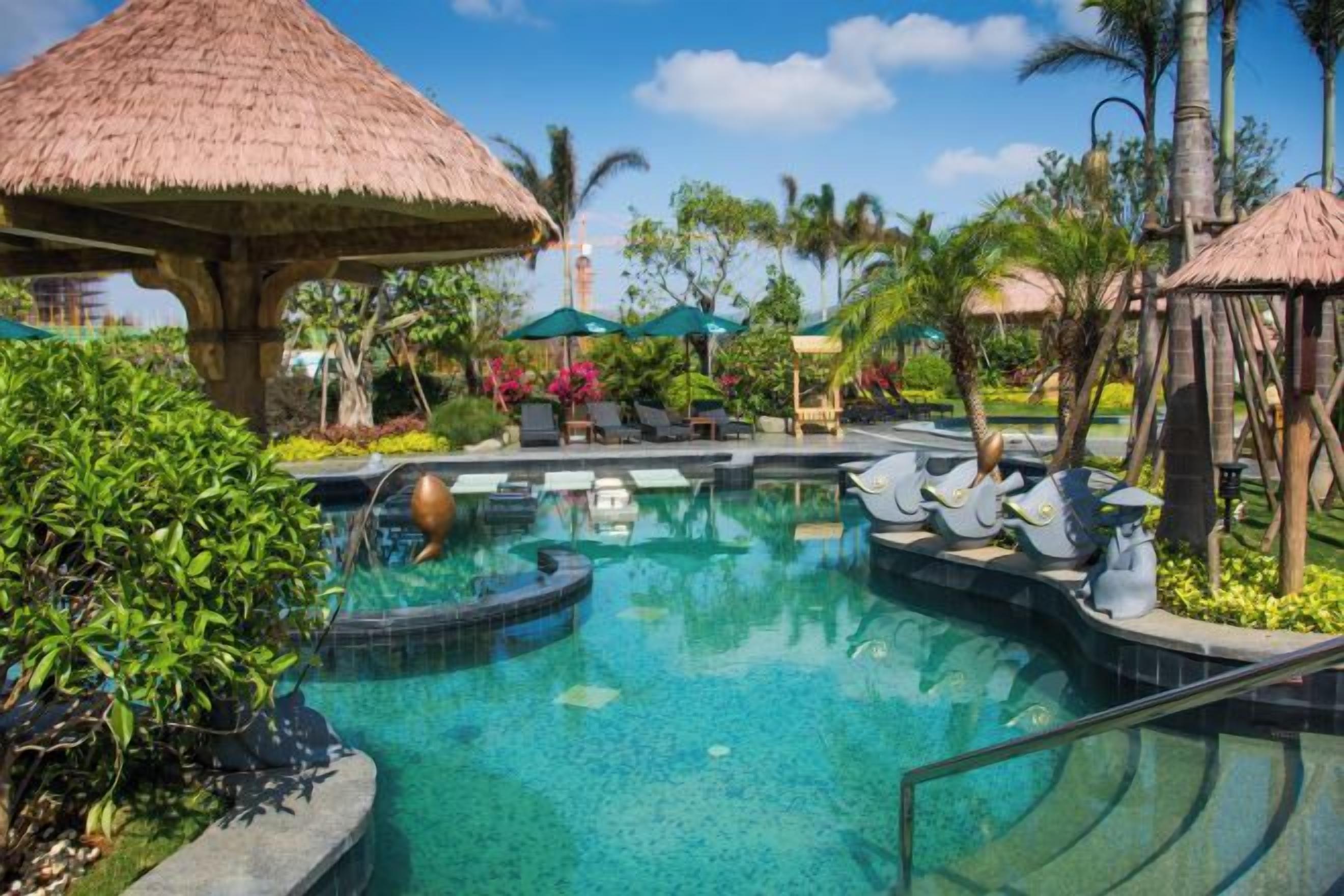A pool area with a thatched-roof structure, lounge chairs, and tropical plants.