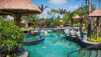 A pool area with a thatched-roof structure, lounge chairs, and tropical plants.