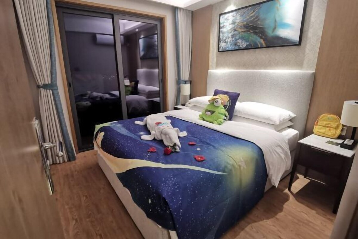Et hotelværelse med en seng, et natbord, en lampe, et billede på væggen og en skydedør til et badeværelse.