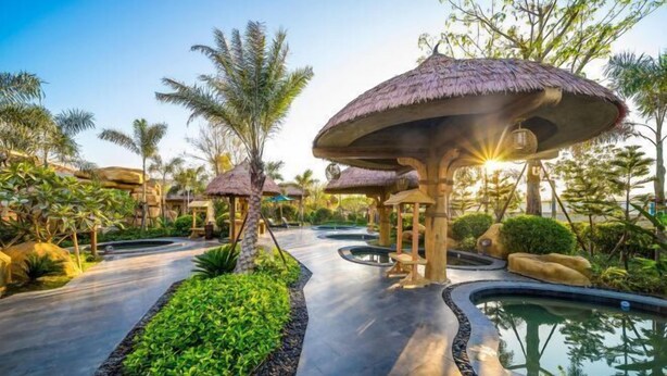 A resort pathway with thatched umbrellas, palm trees, and a water feature. - Amoy Bay Tourist Restort (Zhangzhou)