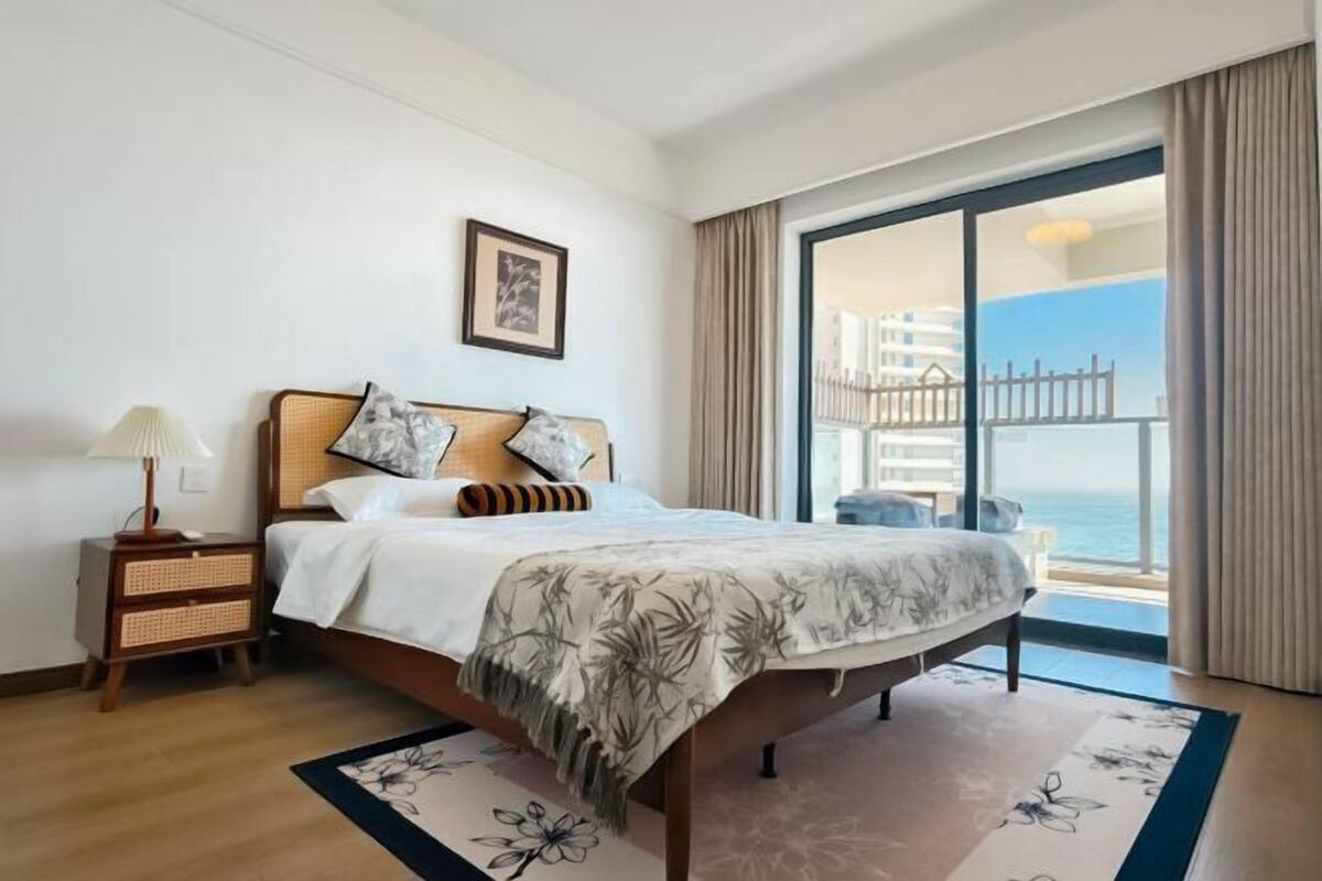 Une chambre d’hôtel avec un lit, une table de chevet, une lampe, un tableau encadré et une vue sur l’océan.