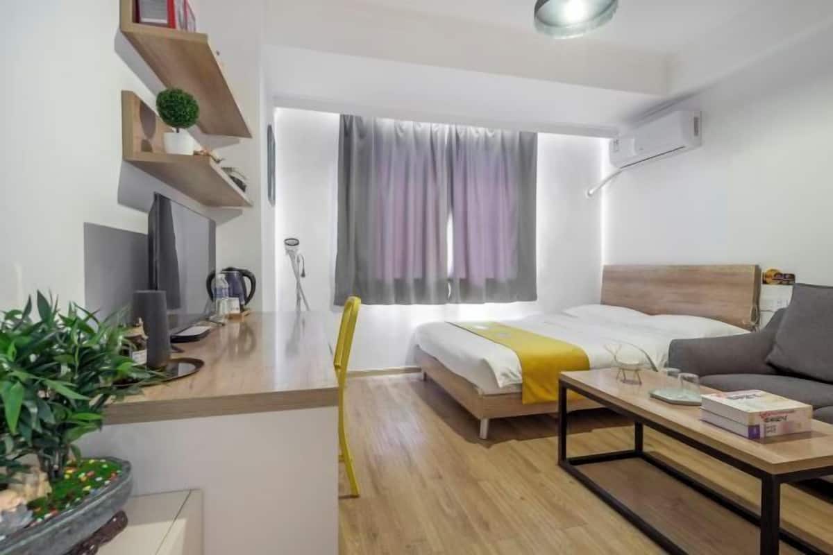 Een moderne hotelkamer met een bed, een bank, een kleine tafel, een televisie en een raam met gordijnen.