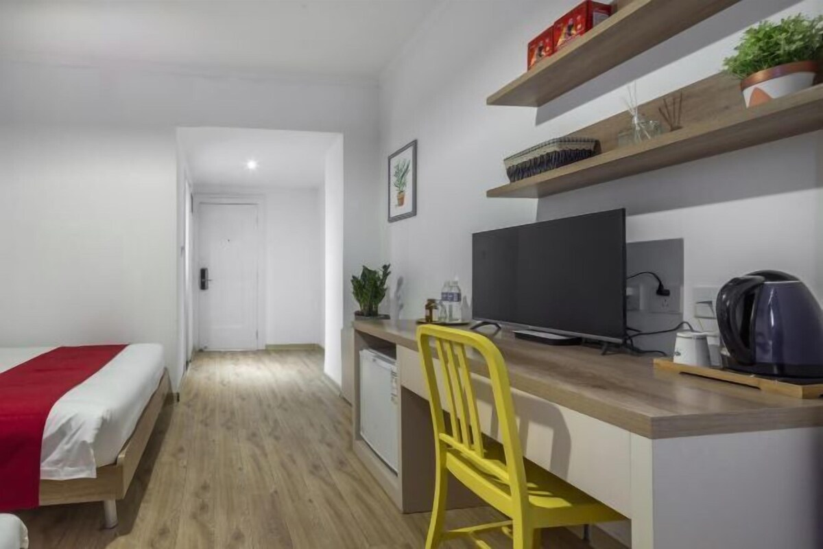 A compact room with a bed, a desk with a chair, a television, and a coffee maker.