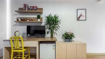 Un espacio habitable compacto con kitchenette, un televisor, un refrigerador pequeño, una silla amarilla y una planta en maceta.