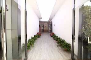 A hallway with a wooden floor, potted plants, and a door on the left. - Product family selection Hotel (Zhengzhou)
