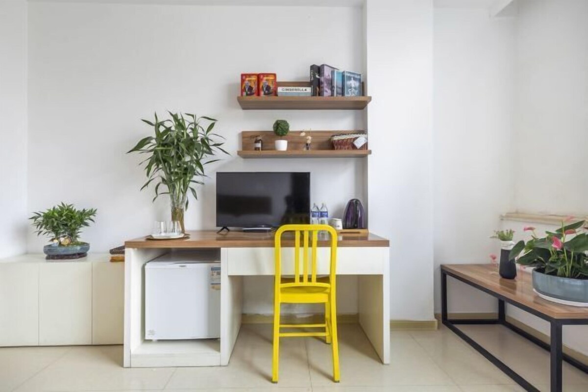 A compact workspace with a desk, chair, television, and shelving with books and decorative items.