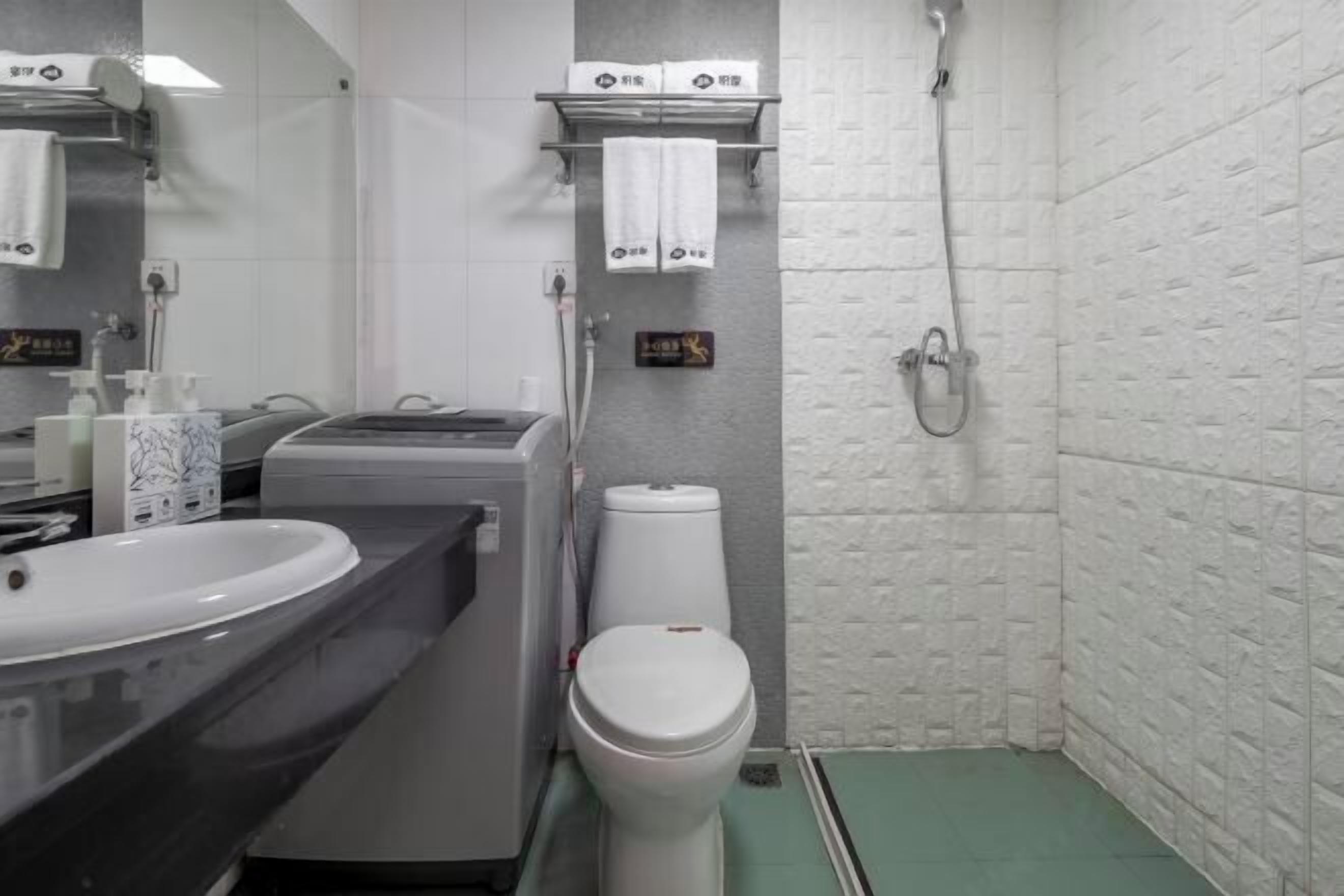 Une salle de bain avec des toilettes blanches, un lavabo et une douche. Des serviettes sont suspendues sur un porte-serviettes et un distributeur de savon est posé sur le comptoir.