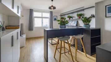 A modern kitchen with wooden flooring, a dark countertop, and two bar stools.