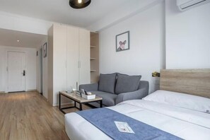 A modern hotel room with a bed, a grey sofa, a small table, and a wardrobe. - Product family selection Hotel (Zhengzhou)