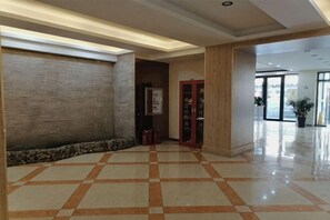 A hotel lobby with a tiled floor, a wooden reception desk, and a large plant. - Home Huayi Hotel(Changchun East Bridge) (Changchun)