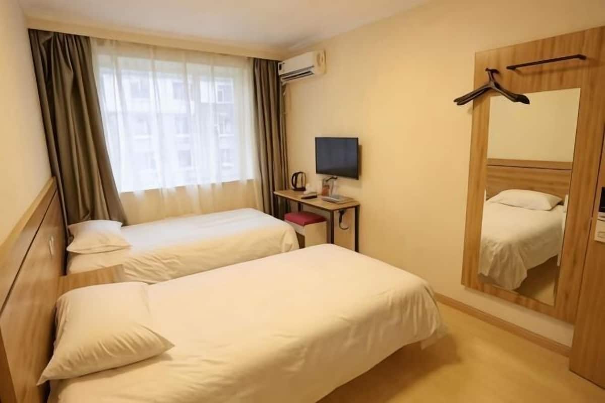 A hotel room with two beds, a TV, a desk, and a mirror.