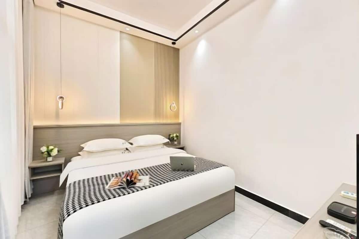 A modern bedroom with a bed, bedside tables, a laptop, and a TV.